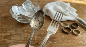 Posate e anelli in argento ossidato e lucidato con rimedi naturali su un tavolo di legno