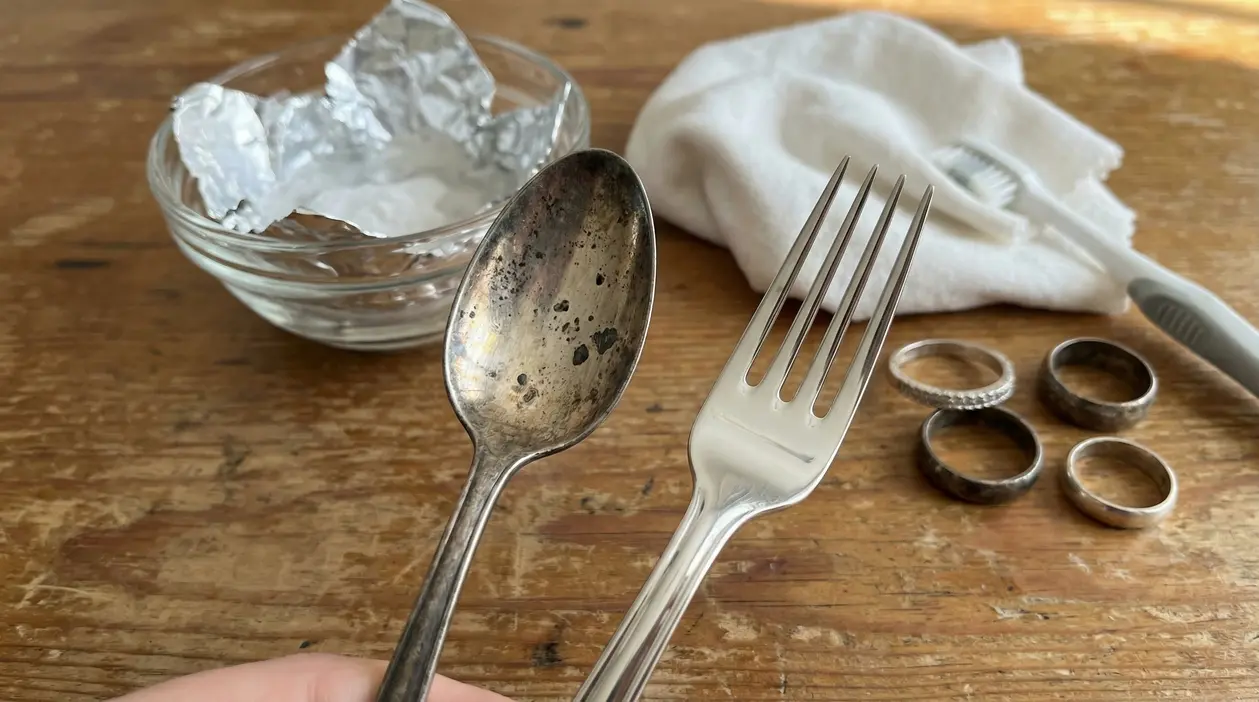 Posate e anelli in argento ossidato e lucidato con rimedi naturali su un tavolo di legno