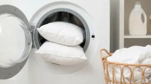 Due cuscini bianchi inseriti in una lavatrice accanto a un cesto della biancheria