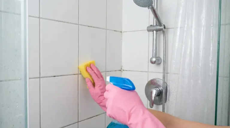 Persona pulisce le piastrelle della doccia con guanti rosa, spugna e spray