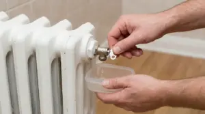 Una persona spurga un termosifone raccogliendo l'acqua con un contenitore di plastica