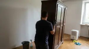 Persona che sposta un armadio in legno lontano dal muro in una stanza luminosa