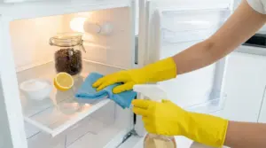 Persona che pulisce un frigorifero con guanti gialli e prodotti naturali