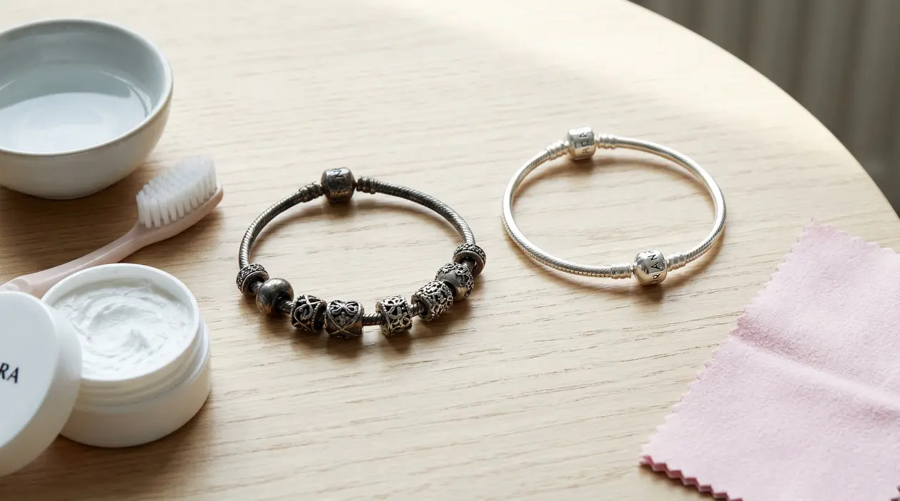 Due braccialetti Pandora, uno ossidato e uno lucido, accanto a prodotti per la pulizia su un tavolo
