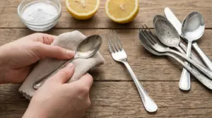 Persona che lucida una posata in acciaio con un panno su un tavolo di legno